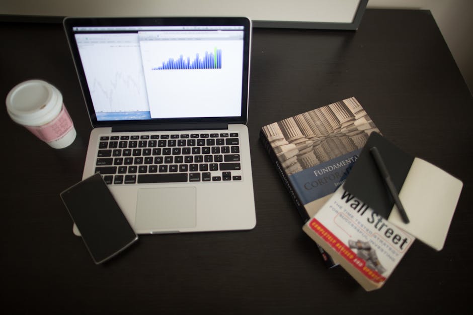 A cozy office desk with a laptop and financial charts under soft lighting.