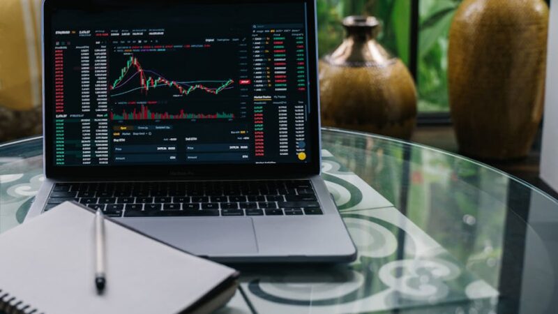 A modern workspace with a laptop, cryptocurrency coins, and a notepad.