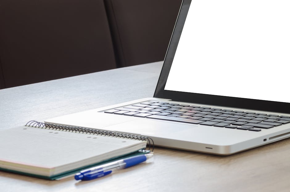 A modern workspace with a laptop, notebooks, and pens in soft light.