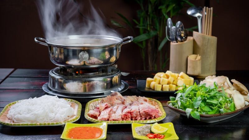 A steaming hotpot with colorful ingredients on a wooden table.