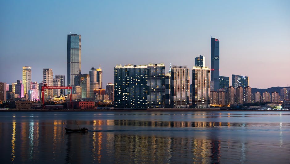 A city skyline at dusk with illuminated buildings and water reflections.