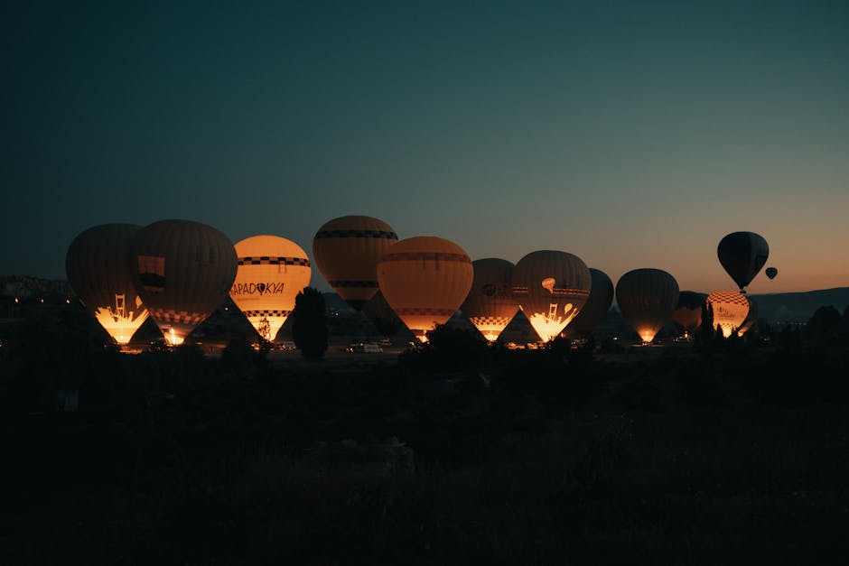 A colorful baseball field at sunset with balloons in the sky.