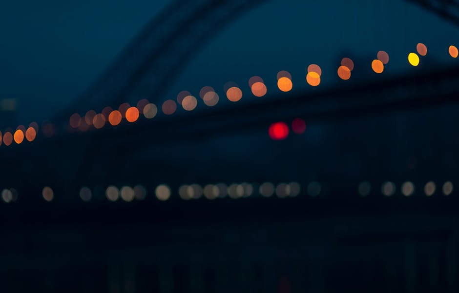 Blurred city skyline at dusk with glowing lights reflecting on water.